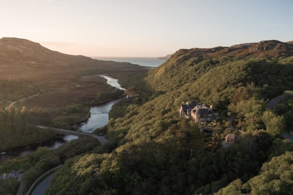 Hope Lodge set among wooded hills above a river, with the sea beyond, in Sutherland