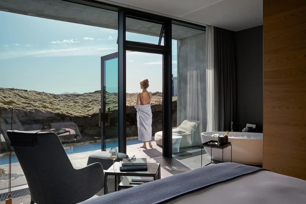 A suite at The Retreat at the Blue Lagoon, looking out through glass doors onto milky geothermal water and moss-covered lava.