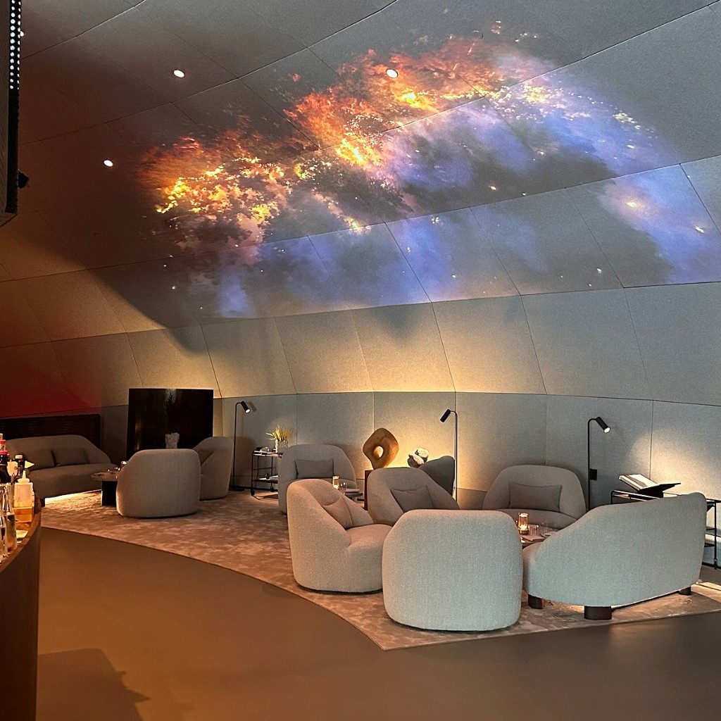 The lounge inside Restaurant Iris at Salmon Eye, with curved panelled walls and a projected sky of colour overhead