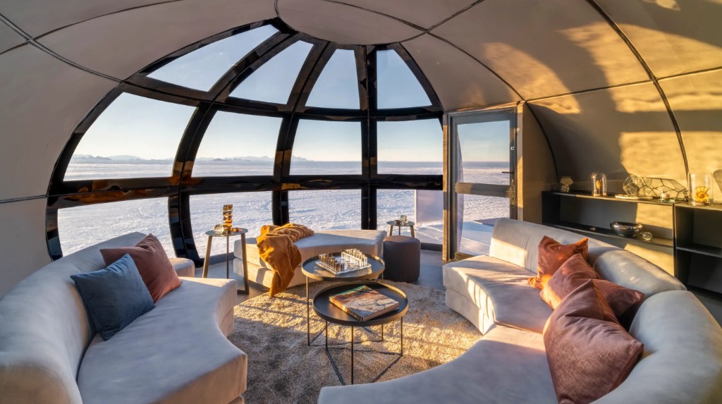 Interior of an Echo Camp pod, with curved sofas facing panoramic windows over Antarctic ice